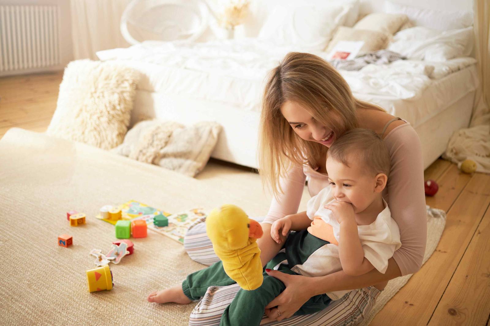 A mother helping her toddler play with blocks on a bedroom floor